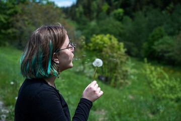 Young hipster girl blows the flower. Pretty girl blowing dandelion in summer park. Cute girl playing with blowball.