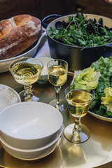 small outdoor dinner party table with vintage glassware filled with white wine, loaf of bread, bowl of salad, pot of steamed mussels with parsley