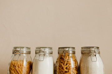 Four glass jars full with dried uncooked food ingredients. Zero waste storage idea for pantry and...