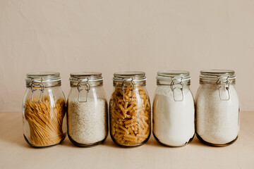 Five glass jars full with dried uncooked food ingredients. Zero waste storage idea for pantry and...