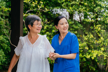 Happy female caregiver in blue scrubs holding hand of senior woman and looking away with smile...