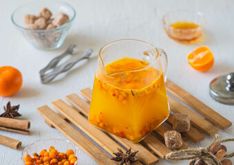 Hot drink, sea buckthorn tea with tangerine slices in a transparent glass teapot on a light concrete background. Hot drink recipes.