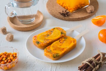 Frozen sea buckthorn briquettes with herbs and tangerine slices for instant hot sea buckthorn tea on a white plate on a light concrete background. Express recipes