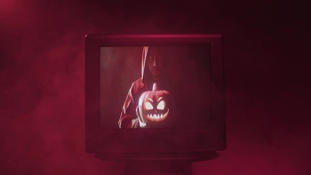 Old tv screen showing Jack-o-lantern close-up. Carved pumpkin on television. Horror film concept, mystery, halloween time. 