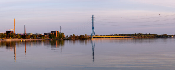 Panoramic view of a powerplant and electricity pylon casting relflections on the calm water during the sunset