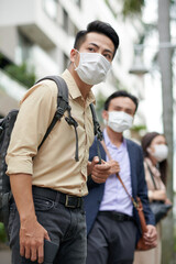 Fototapeta premium Hurrying anxious young Asian man in protective mask waiting for taxi or bus