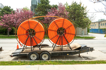 Large spools of smooth walled HDPE plastic cable (orange) conduit on trailers waiting to be...
