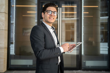 Fototapeta premium Uses a tablet writes a message to a client a man in glasses and a formal suit a businessman