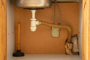 A plunger stands in a cupboard under the sink in the kitchen, cleaning clogged pipes, pipe cleaner