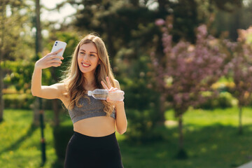 Naklejka na ściany i meble Sporty young girl with phone take selfie photo in the park