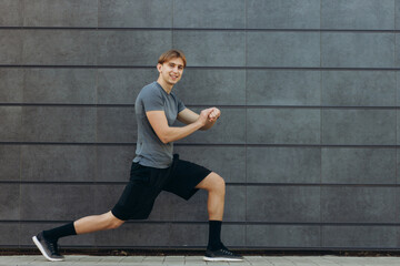 Young man doing stretching exercises against black wall