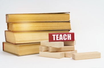 On a white surface, a stack of books and wooden blocks, on a red block there is an inscription - TEACH