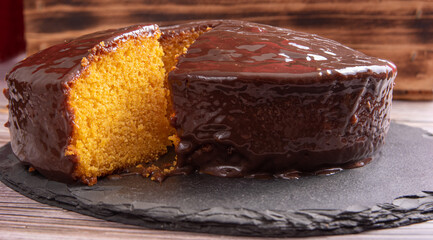 Sliced ​​carrot cake, covered in chocolate on stone surface over rustic wood, selective focus.