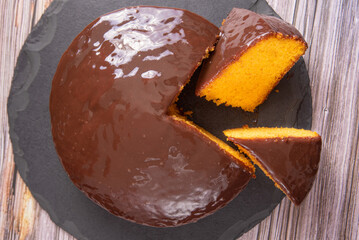 Sliced ​​carrot cake, covered in chocolate on stone surface over rustic wood, top view.
