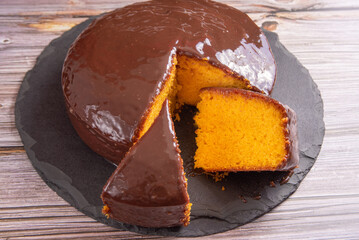 Sliced ​​carrot cake, covered in chocolate on stone surface over rustic wood, selective focus.