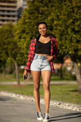Beautiful young hot black woman in jeans shorts posing in hot summer sunshine.