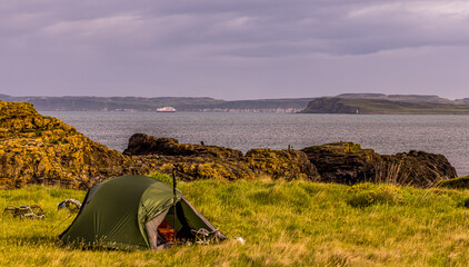 Camping tent om the County Antrim coast as a cruise passenger ship arrives at Church Bay, Rathlin Island, Ballycastle, Northern Ireland, Causeway Coast and Glens Coastal route