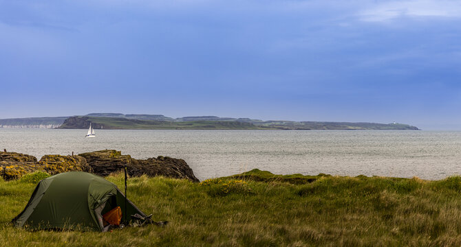 Camping tent with Rathlin Island and a sailing boat backdrop, Fairhead, County Antrim, Northern Ireland