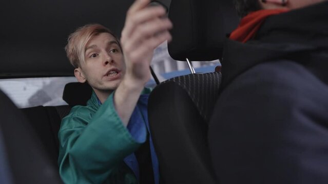Young man with pink hair in in mint green coat emotionally asks for stop and shows direction with his hand, arguing with a taxi driver. Slow motion 4k footage