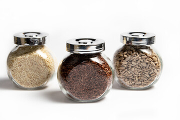 Glass jars with sesame seeds flax seeds sunflower seeds on white background