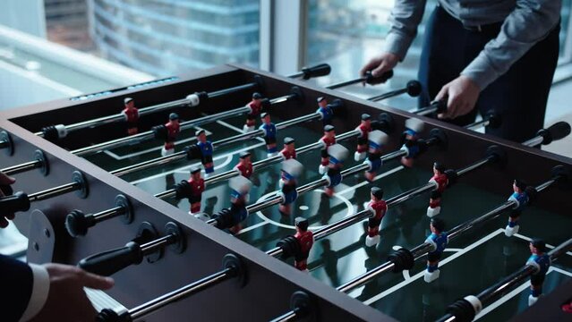 Office workers take a break from routine work with a table game of football. Close-up of a man twisting a handle making a football player figurine spin in a game