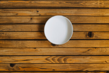 A round cardboard white empty box stands on a wooden background.