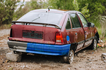 An old, beautiful red broken, discarded car stands in a landfill with punctured wheels after the war in Ukraine.