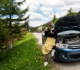 Caucasian hipster girl using a mobile phone to call the mechanic while looking at broken down car on street. Young girl with a broken car on the road call service. Cute girl near a broken car