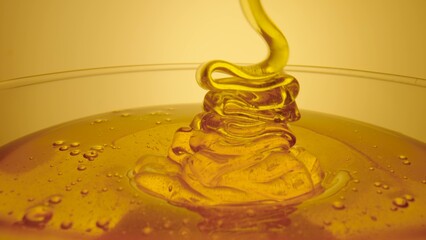 Thick golden honey flowing into a glass. A jet of fresh organic honey molasses pours close up. Sweet product of beekeeping. Healthy dessert, sweet food, natural syrup spilled.