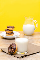 Mini donuts covered with chocolate glaze served with bottle, jug, glass of milk. Stack of tasty sweet sugar creamy or icing doughnuts dessert food on plate and napkin on kitchen. national donuts day