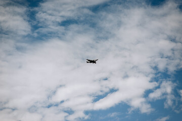 A large military supersonic fighter plane with missiles flies low in the blue sky with clouds.