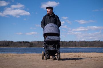 Grandfather walking with a baby stroller on cold and gloomy spring day