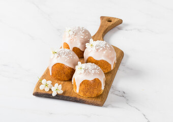 Small cute Cakes with white sugar glaze, decorated with a flower and confectionery sprinkles, on a wooden board. Light background