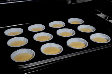 Twelve uncooked cupcakes, muffins in muffin tin in electric oven. Homemade bakery, food, cooking, pastry, semi-finished products and raw concept