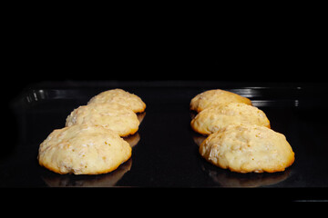 Process of cooking six homemade crunchy oatmeal cookies on metal sheet in oven - front view....