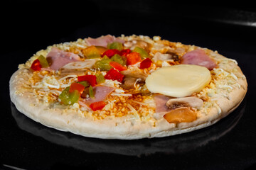 Uncooked pizza with sausage, mushroom, pepper, mozzarella on tray in electric oven, black background. Italian cuisine, homemade bakery, fast food, cooking, semi-finished products and raw concept