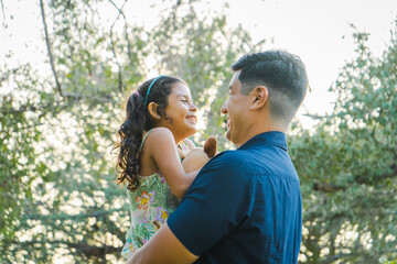Fototapeta premium Mexican Girl Smiling at Dad, Hugging in the Park