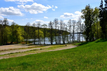 Naklejka premium View of a beautiful and well maintained public park including a number of rocks, boulders, stones, benches, and paths located next to a dense forest or moor, as well as to a river bank seen in summer 