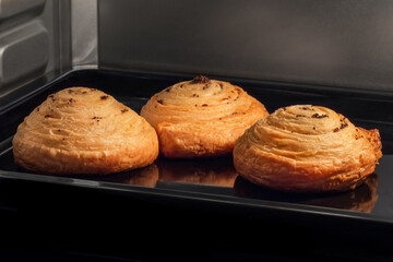 Three baked buns with poppy seeds on tray in electric oven. Homemade bakery, food, cooking and pastry concept
