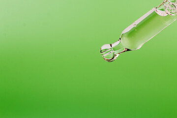 Dripping essential oil or serum from pipette on green background macro image. Eco, natural cosmetics concept, selective focus, close up image