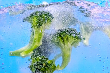 Falling fresh broccoli into water with splash and bubbles. Selective focus, clos up image.