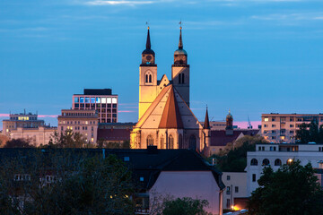 Fototapeta na wymiar Beleuchtete Johanniskirche in Magdeburg überragt die umstehenden Gebäude der Landeshauptstadt von Sachsen-Anhalt im goldenen Licht an einem Abend im Frühling