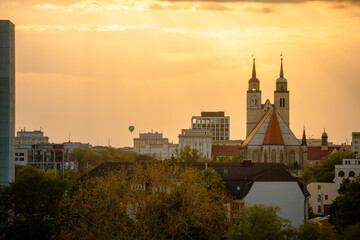 Naklejka premium Magdeburg Skyline - Heißluftballon über der Landeshauptstadt von Sachsen-Anhalt, Magdeburg am Fluss Elbe, im Sonnenuntergang mit Johanniskirche, Blauer Bock, Ulrichshaus, Bäume und Wälder