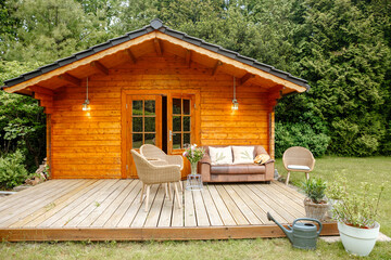 Leather sofa on a terrace outside next to a wooden house. Wooden garden house with outdoor seating. Relaxation in the garden. wooden hut