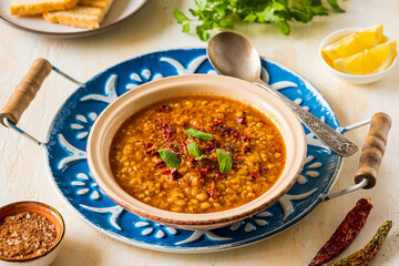 Red lentil and bulgur bride soup in a clay bowl on a light concrete background. Turkish cuisine. Recipes lentils, legumes