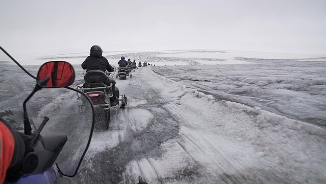 Aroup of tourists riding snowmobiles with a guide at Vatnajokull glacier in Iceland. Active sport, recreation, lifestyle.