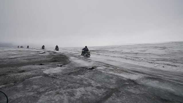 Aroup of tourists riding snowmobiles with a guide at Vatnajokull glacier in Iceland. Active sport, recreation, lifestyle.