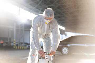 Man dressed white protective overalls spraying surface antibacterial sanitizer sprayer during...