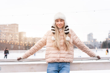 Beautiful lovely middle-aged girl blonde hair warm winter jackets knitted glove stands ice rink background Town Square. Christmas mood lifestyle