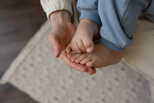 Crop mom touching foot of cute kid at home
